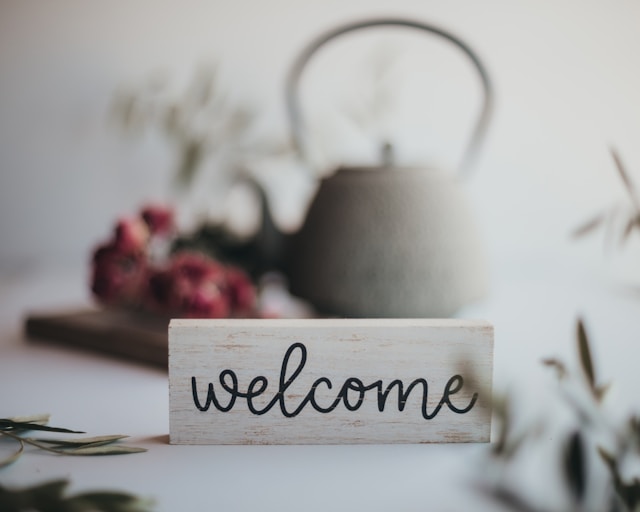 A wooden block printed with the word “Welcome” sits on a table. 
