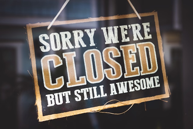 A sign that says “Sorry we’re closed but still awesome) hangs on a glass door.
