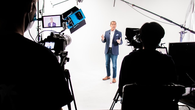 A man stands against a white background and in front of multiple cameras for a live broadcast. 
