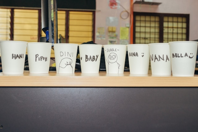 A line of white paper cups printed with people’s names. 
