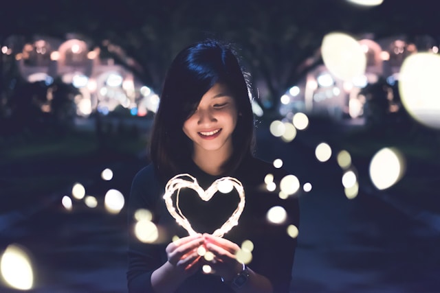 A young woman holds a wire of lights shaped into a heart.