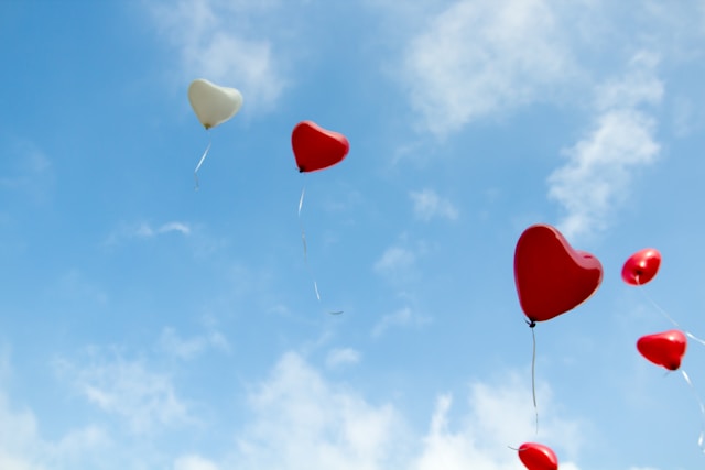 Red and white heart-shaped balloons float away in the sky. 
