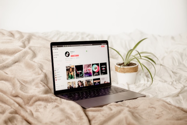 A laptop on a bed displays the TikTok profile in a browser.
