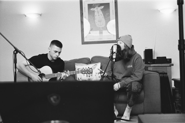 A man plays the guitar beside a woman who sings into a microphone. 
