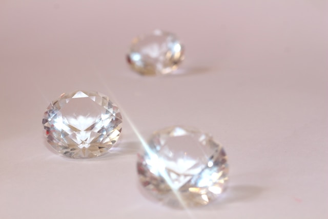 Three cut diamonds sit on a pink table. 
