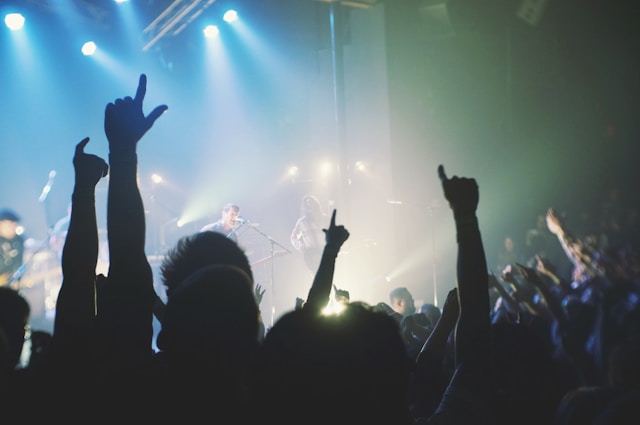 Viewers at a live concert raise their hands and cheer for the performers on stage.
