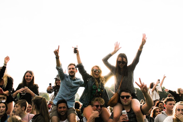 Some members of the audience at an outdoor event sit on the shoulders of their friends for a better view. 

