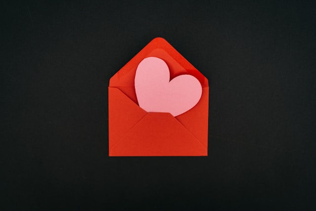 A pink paper heart inside a red envelope. 