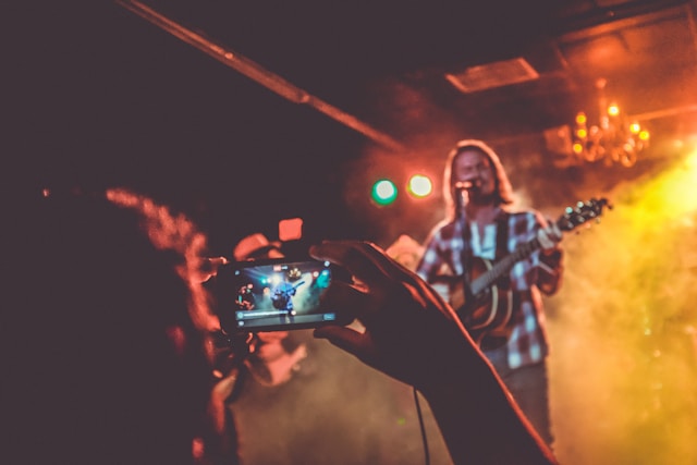 An audience member uses their phone to record a video of a musician on stage.
