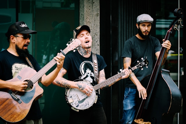 Three street performers play instruments and sing for a crowd. 
