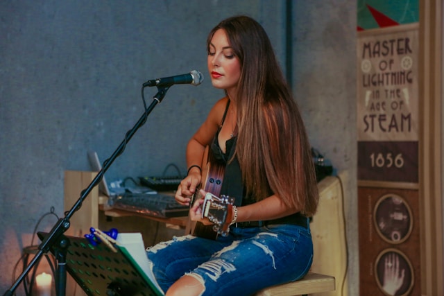 A woman plays the guitar and sings on a microphone. 