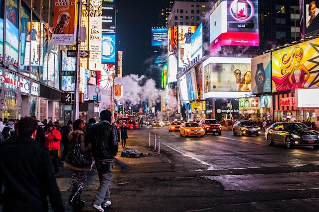 A busy street at night with big and colorful ads on the sides of tall buildings. 
