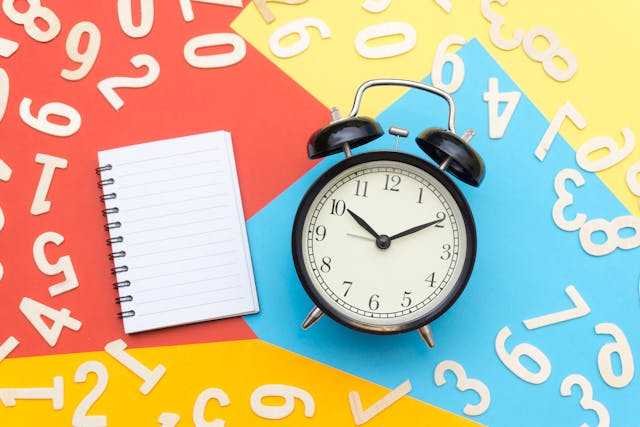 An alarm clock and a book on a multicolored surface with digits.
