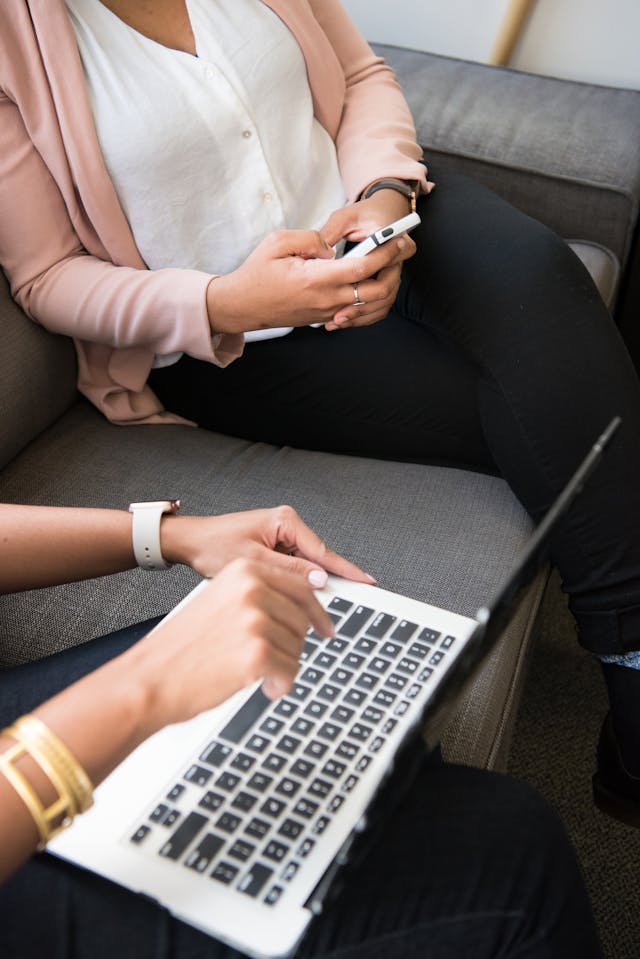 A woman uses her phone next to a person using a laptop.
