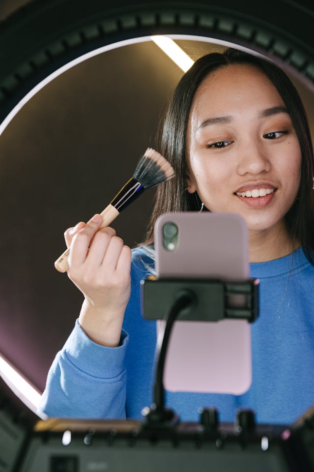 A woman records herself applying makeup with a makeup brush.
