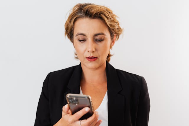 A woman looks at her phone with a surprised expression.
