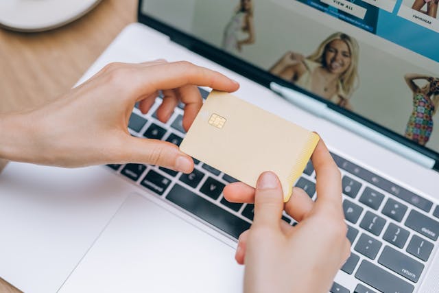 A person holds their credit card over a laptop.
