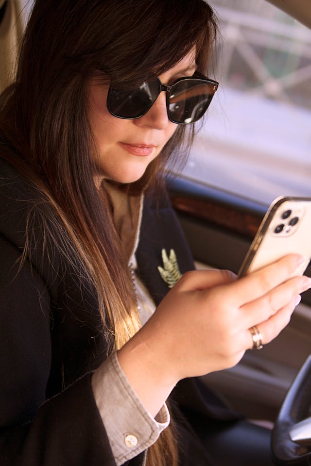 A woman in sunglasses types on a cell phone.
