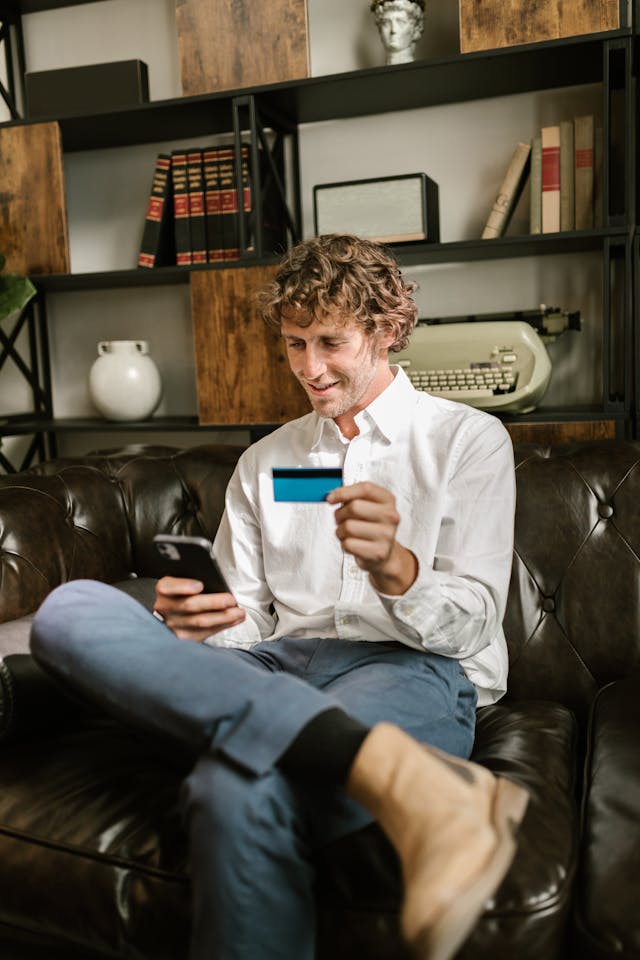 A man holds his card while typing on his phone.
