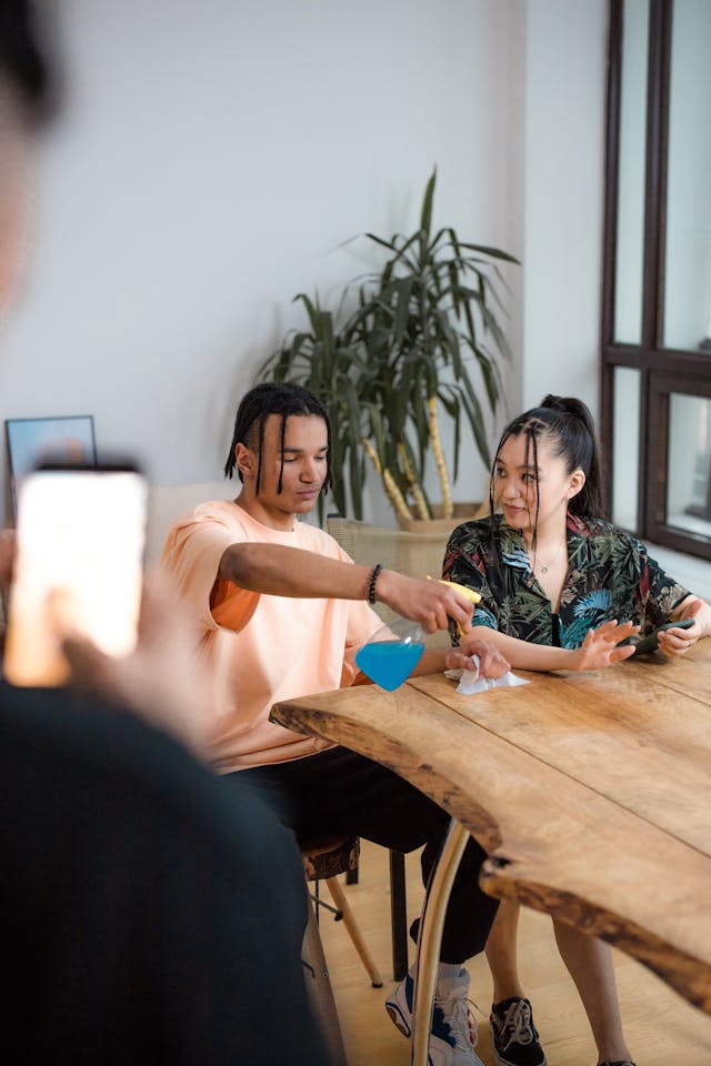 Someone records two people sitting at a wooden table.