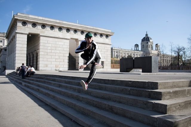 A street dancer performs a high jump over concrete steps. 
