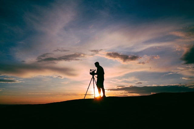 The silhouette of a man and his video camera on a tripod against the sunset. 
