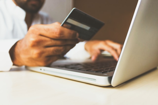 A man enters his credit card information into his laptop. 
