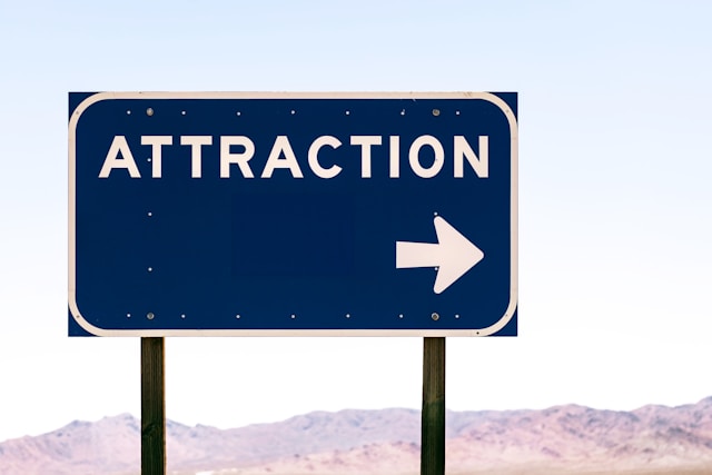 A blue road sign that says “Attraction” in white beside a white arrow. 
