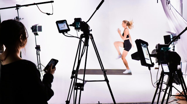 A fitness trainer performs a workout routine in front of cameras. 
