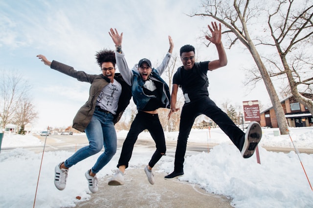 A group of three friends jump up together while laughing.