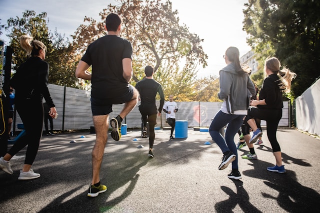 A small group of people performs cardio exercises at the park. 
