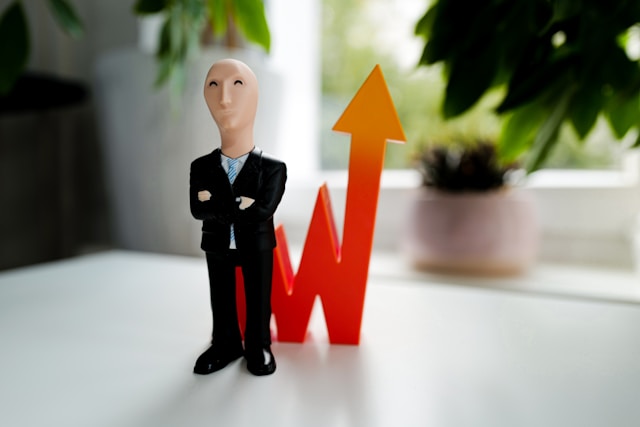 A figurine stands in front of a spiking trend arrow.
