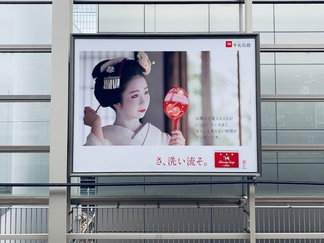 A billboard on a walkway features a Japanese lady wearing white makeup and a kimono. 
