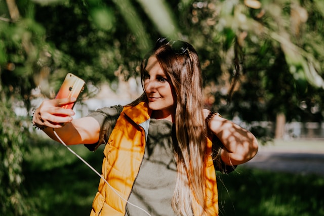 Woman standing outside, holding a plugged-in iPhone taking a selfie video for TikTok