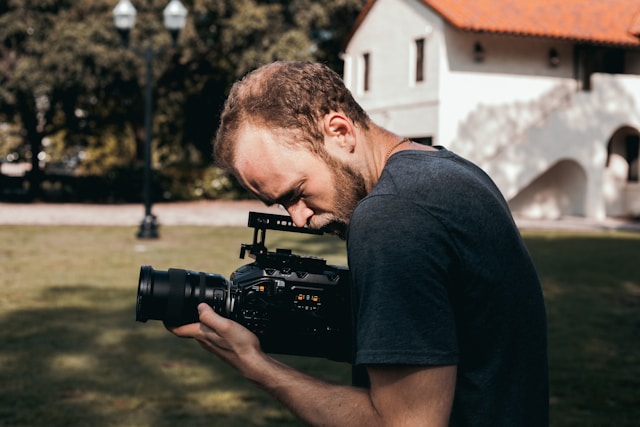 A man carries a DSLR camera and records scenes at a park. 