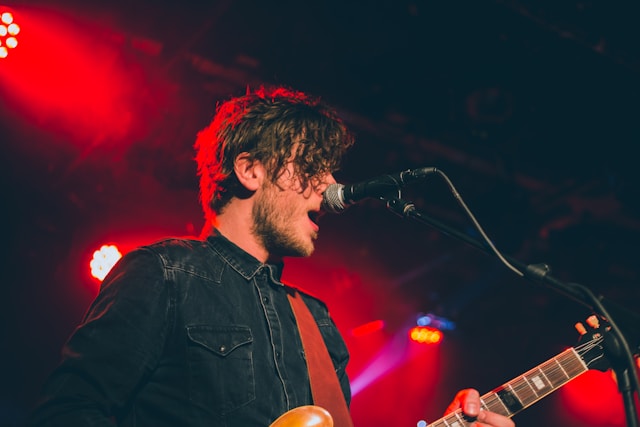 A musician plays the guitar while singing into a microphone. 
