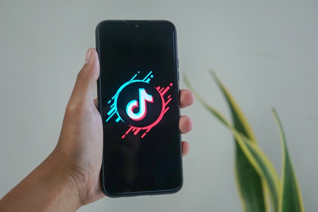 Someone holds a smartphone that shows a stylized TikTok logo.
