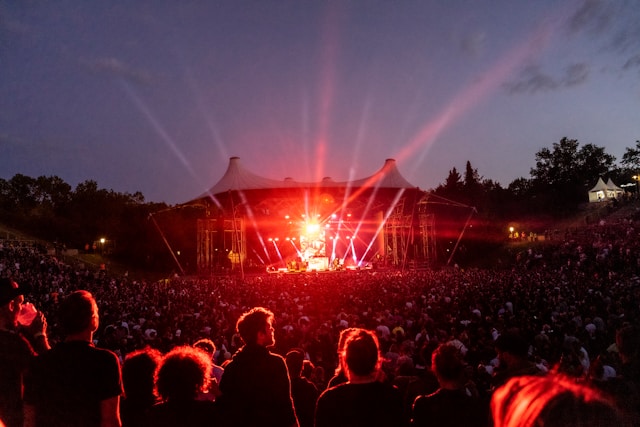 Stage lights at an outdoor event illuminate a massive audience surrounding the stage. 
