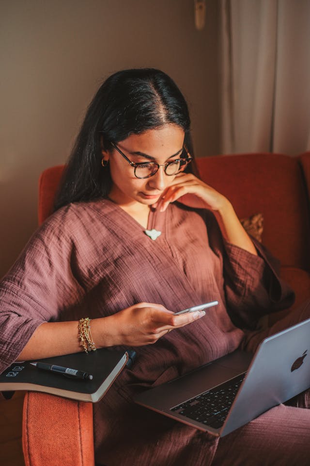 A woman leans back in an armchair while she uses her phone.
