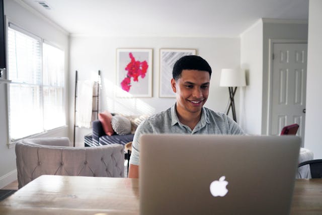 A man types on his laptop while sitting at a table.
