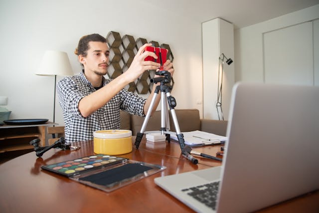 A man sets up his red phone on a tripod.
