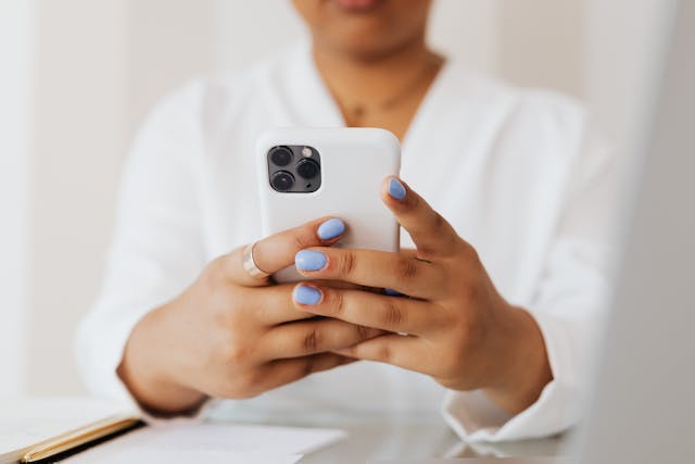 A person in a long-sleeve, white, button-down shirt types on their cell phone.
