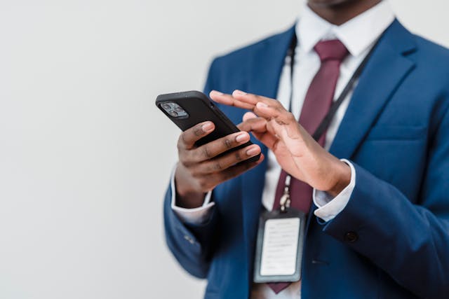 A man in a business suit scrolls on his cell phone.
