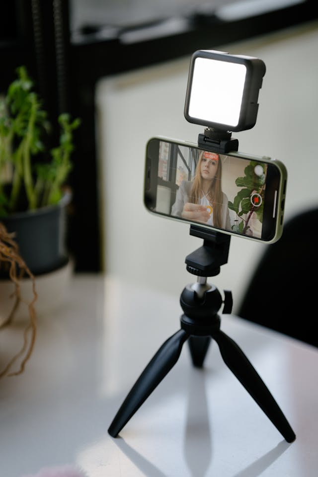 A phone on a tripod shows a woman applying makeup.
