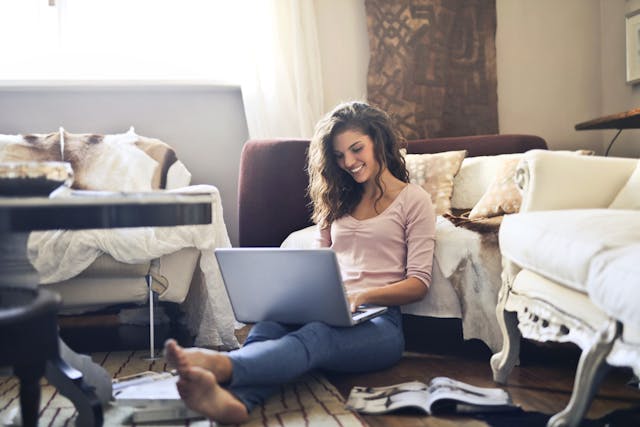 A woman sits on the floor while she types on her laptop.