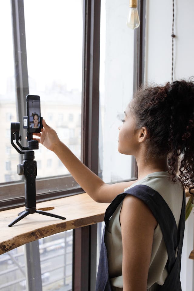 A woman adjusts a camera mounted in front of a window.
