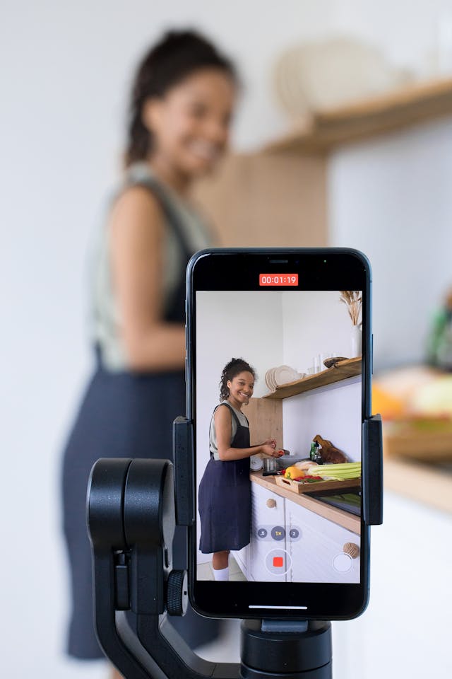 A phone records a woman cooking in the kitchen.
