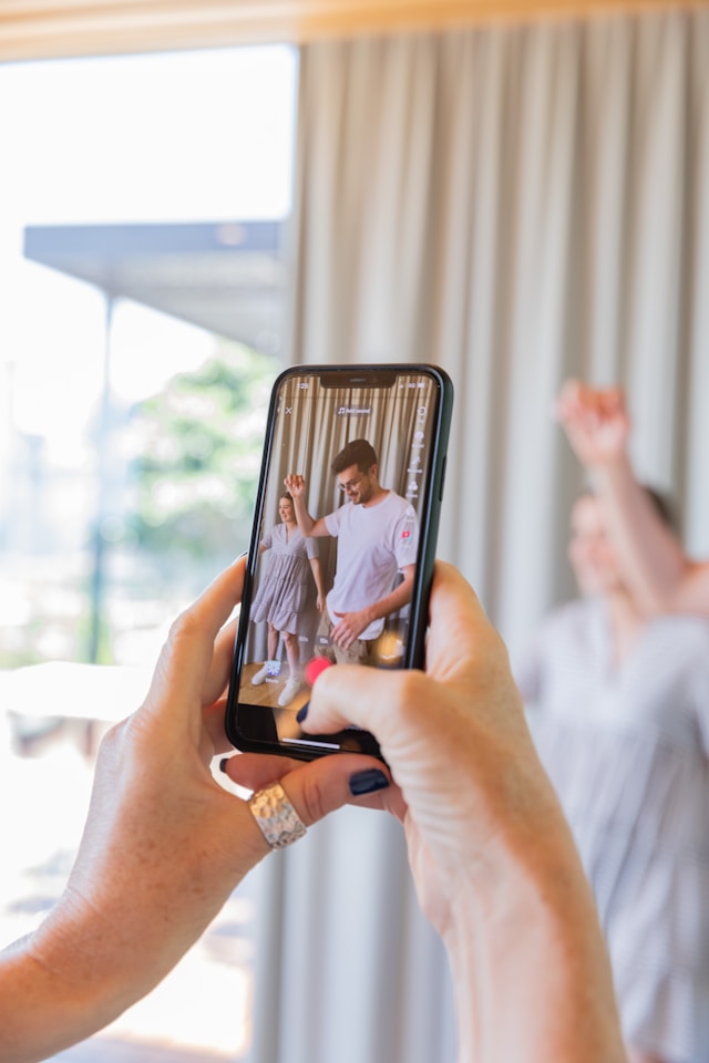 Close up of hands holding a phone, filming a TikTok of a man and a woman dancing.