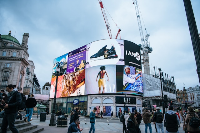 A busy street with a tall building covered with big and colorful ads.