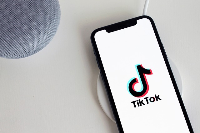 A phone on a white surface displays the TikTok logo.
